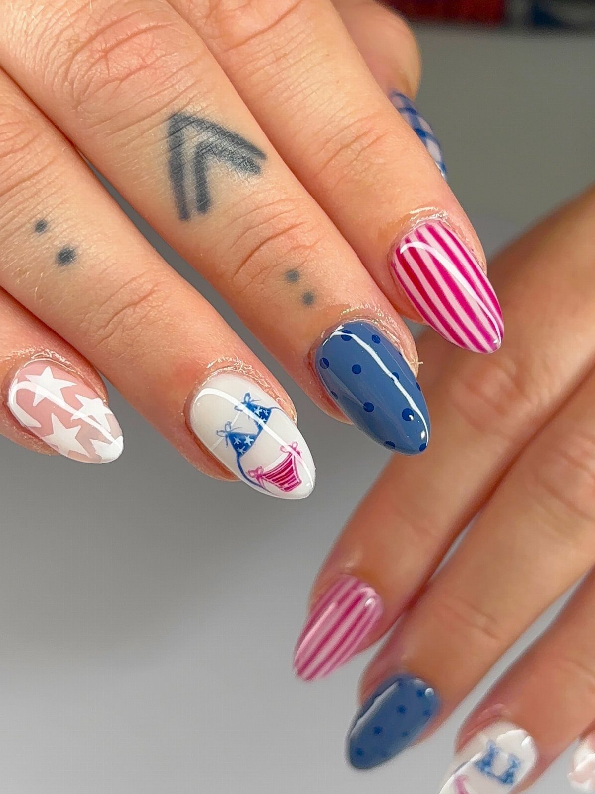 Almond-shaped nails with red, white, and blue patriotic patterns and a bikini illustration.