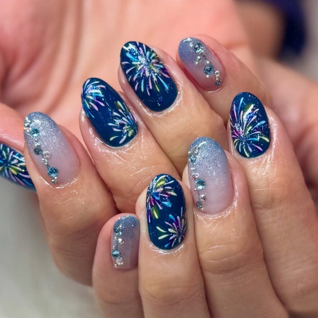 Nail art featuring dark blue nails with colorful firework bursts and silver glitter.