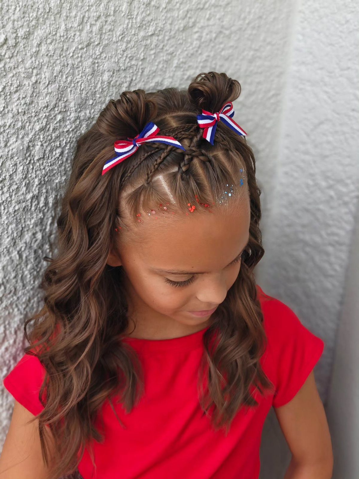 Young girl with curly brown hair in buns with red white and blue ribbons