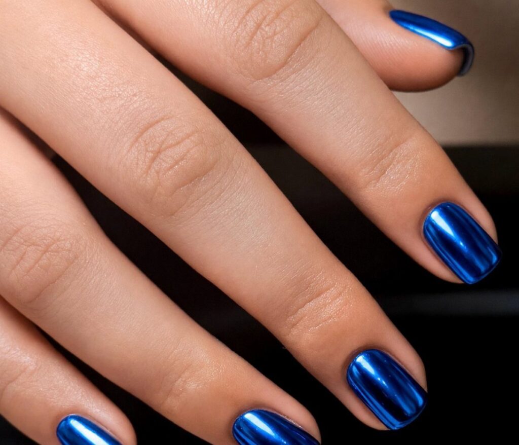 Metallic blue chrome acrylic nails on a hand against a dark background.