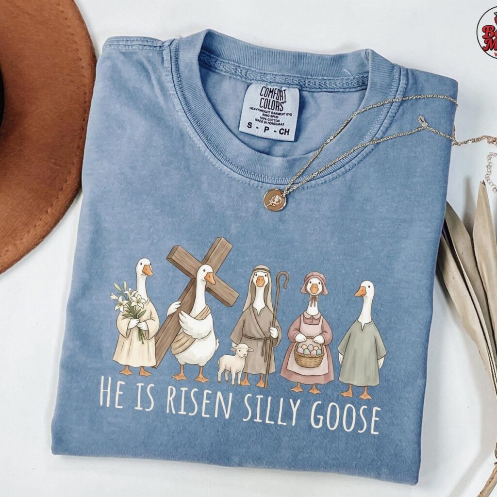 Light blue t-shirt with geese illustration and religious pun laid on white background.