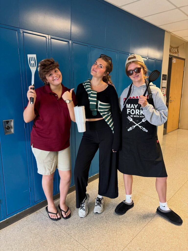 Three students in a school hallway dressed in BBQ dad themed spirit week outfits.