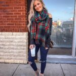 Woman wearing a dark sweater and red plaid scarf with ripped blue jeans.