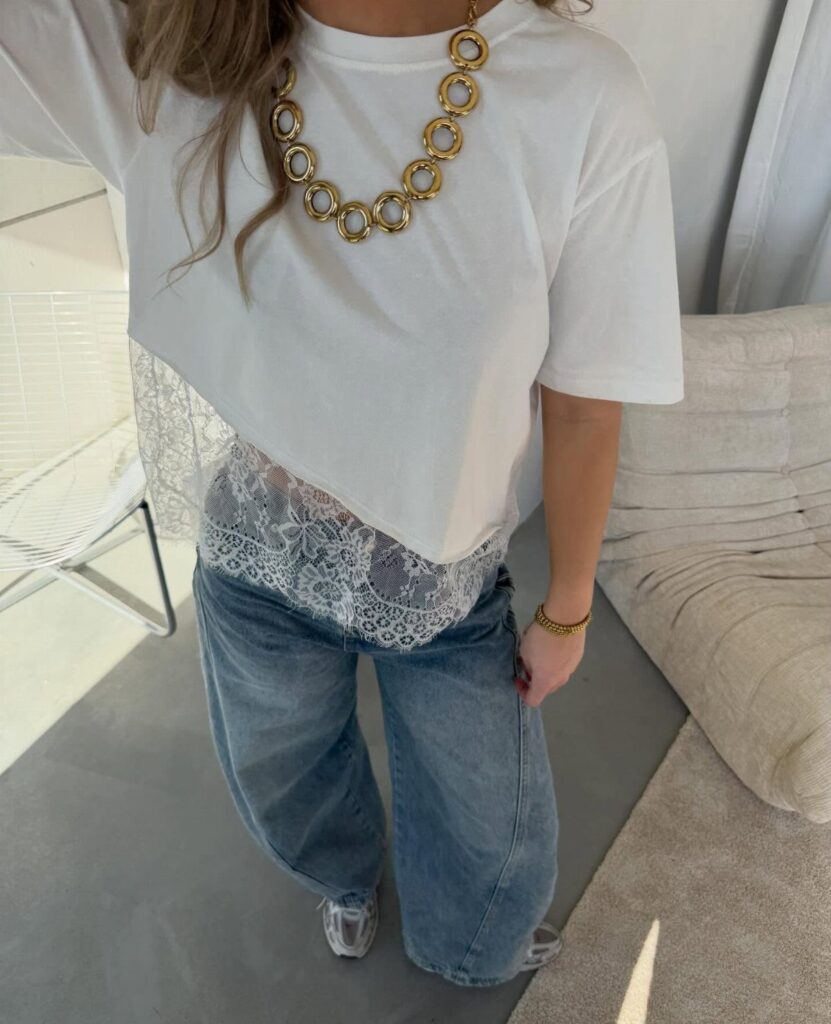 Woman wearing a white lace-hemmed t-shirt, blue wide-leg jeans, and gold chain necklace.