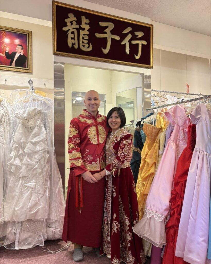 Couple wearing red traditional Chinese wedding attire posing in a bridal clothing store