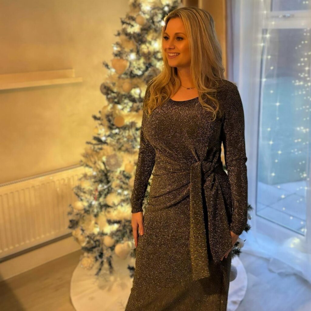 Woman in a shimmering metallic gold wrap dress standing by a Christmas tree