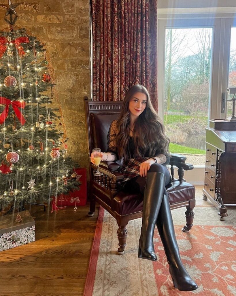 Woman in a short plaid dress and black over-the-knee boots by a Christmas tree