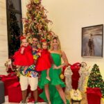 Family posing by a Christmas tree wearing red dresses and a green dress.
