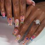 Colorful floral nail art with gemstones on long square nails and a diamond ring.