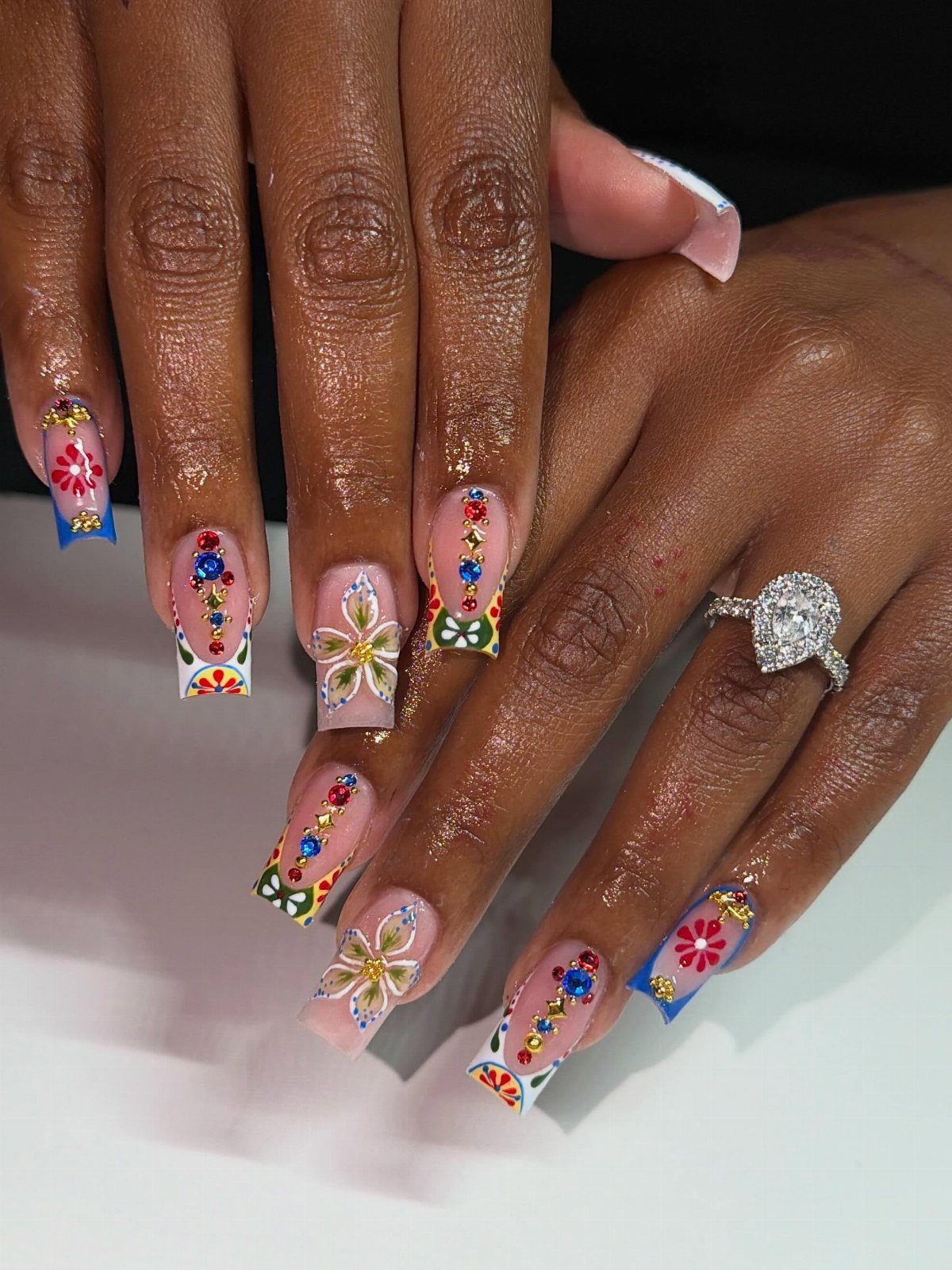 Colorful floral nail art with gemstones on long square nails and a diamond ring.
