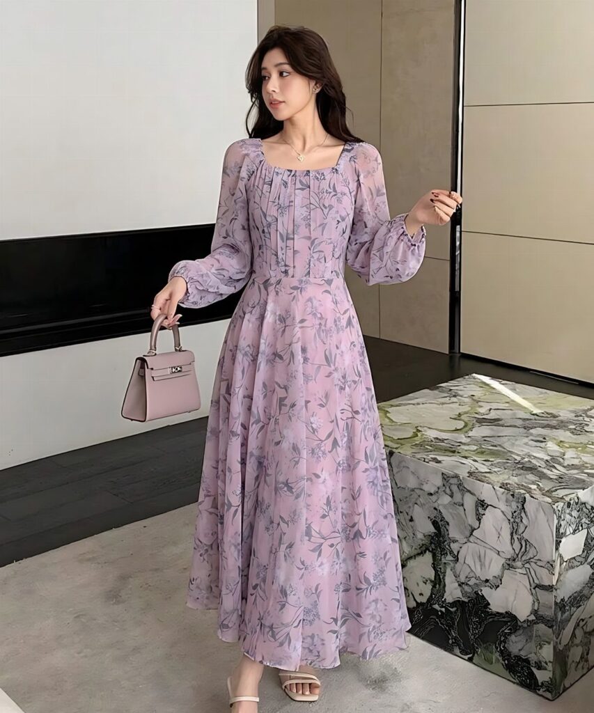 Woman in a purple floral chiffon maxi dress holding a small purple handbag.