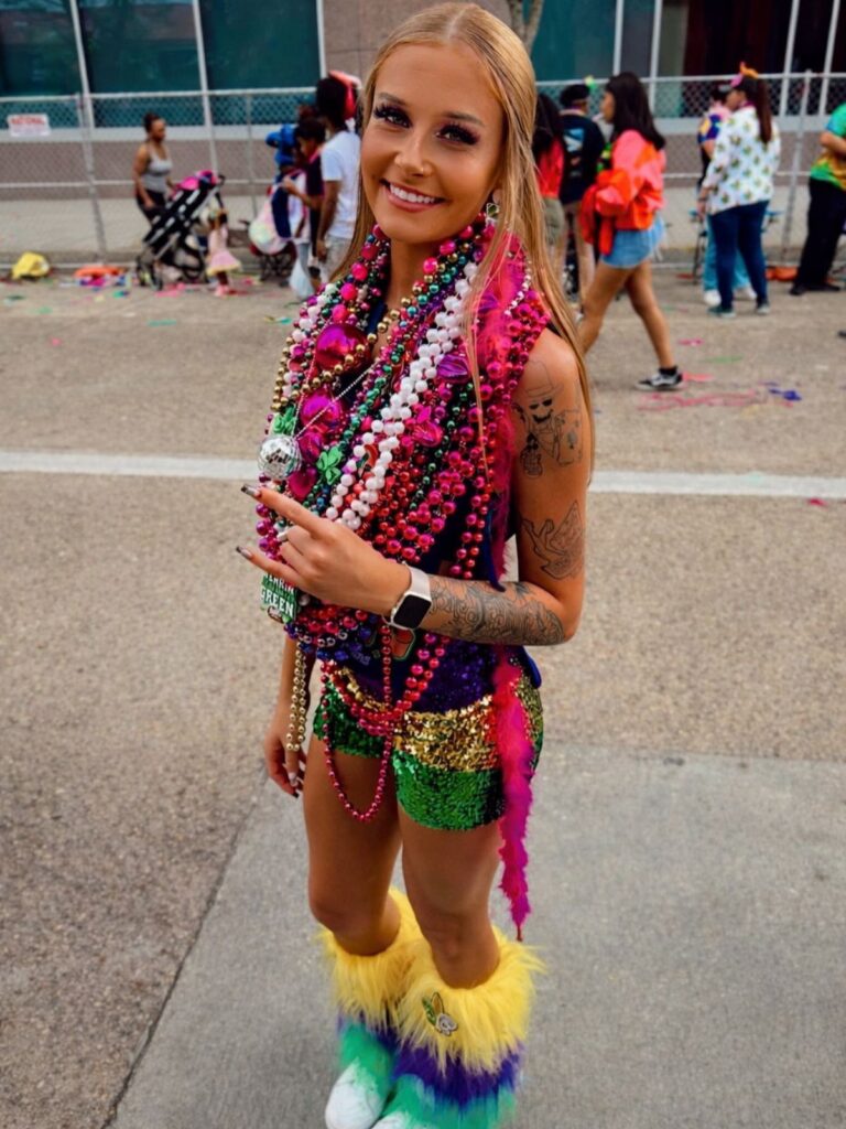 Woman in sequined purple and green outfit with colorful beads and feathered boots.