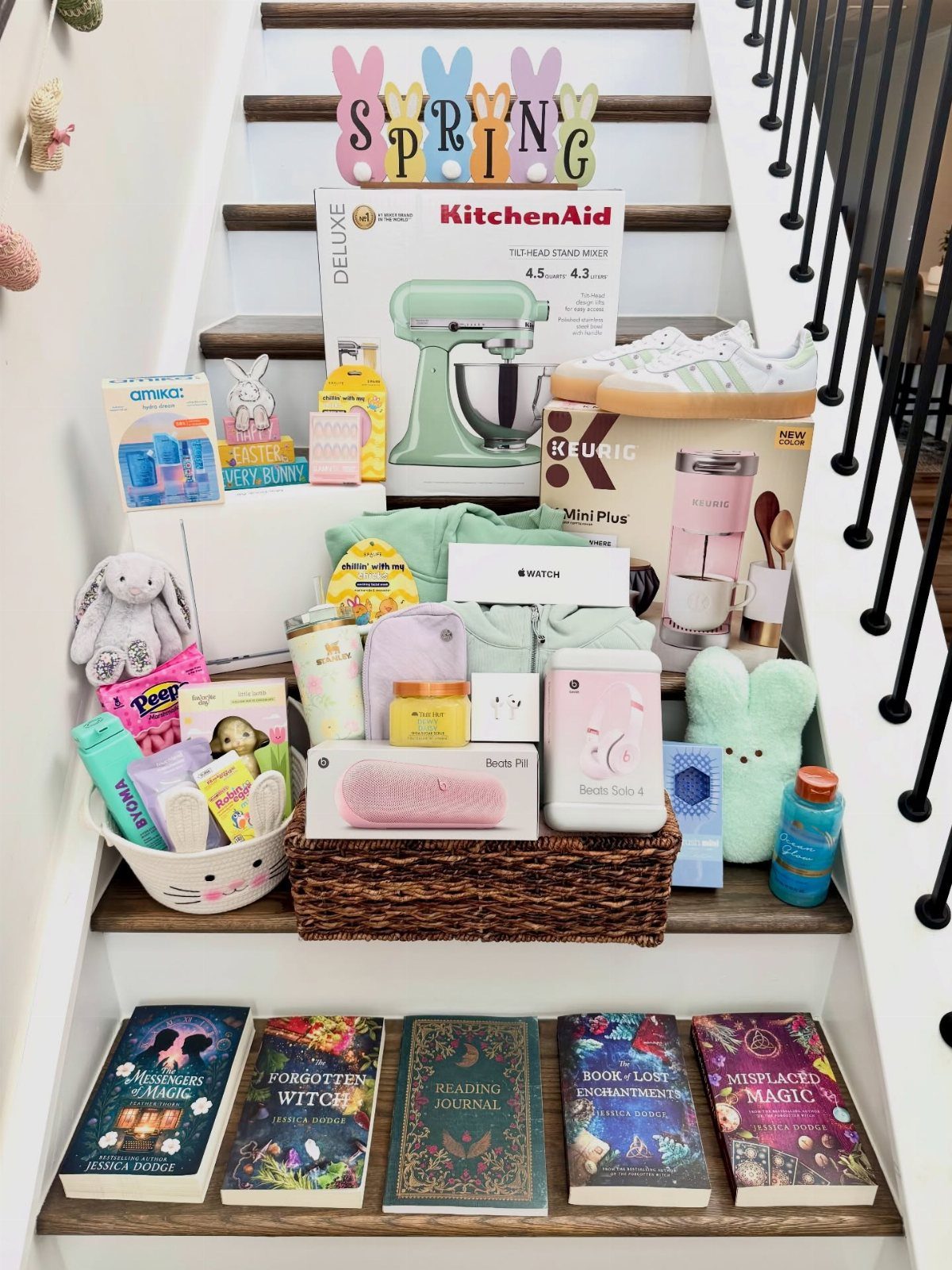 Assorted adult Easter gifts including a mixer and books arranged on white stairs.