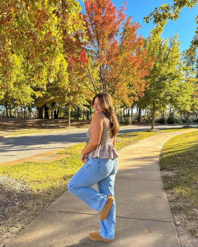 Woman in plaid peplum top and wide-leg jeans standing on autumn sidewalk