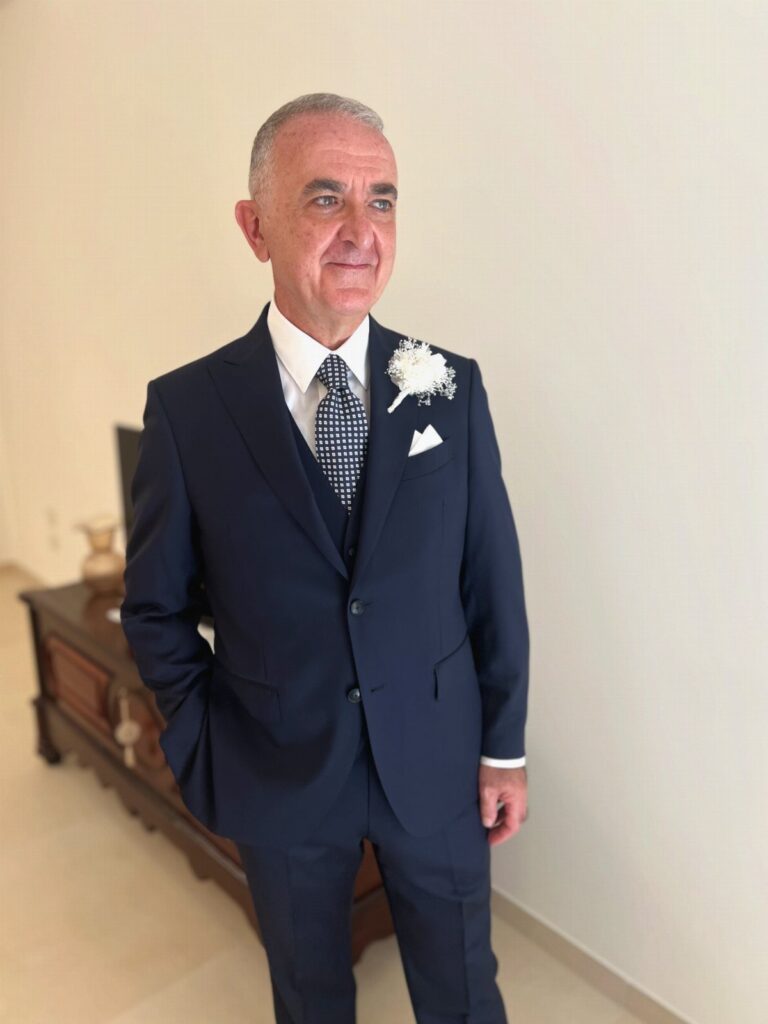 Man in a navy blue three-piece suit with a white floral boutonniere.