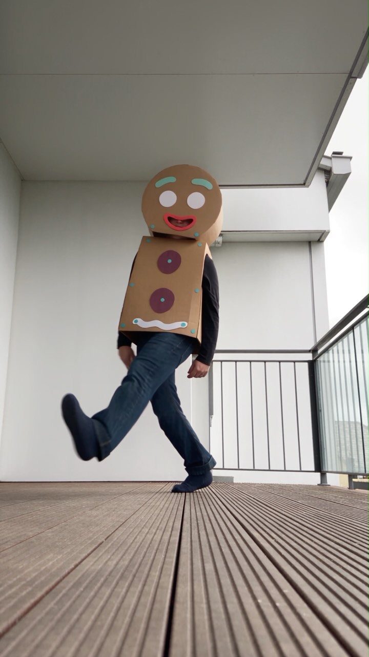 Person in a homemade brown cardboard gingerbread man costume walking on a wooden deck