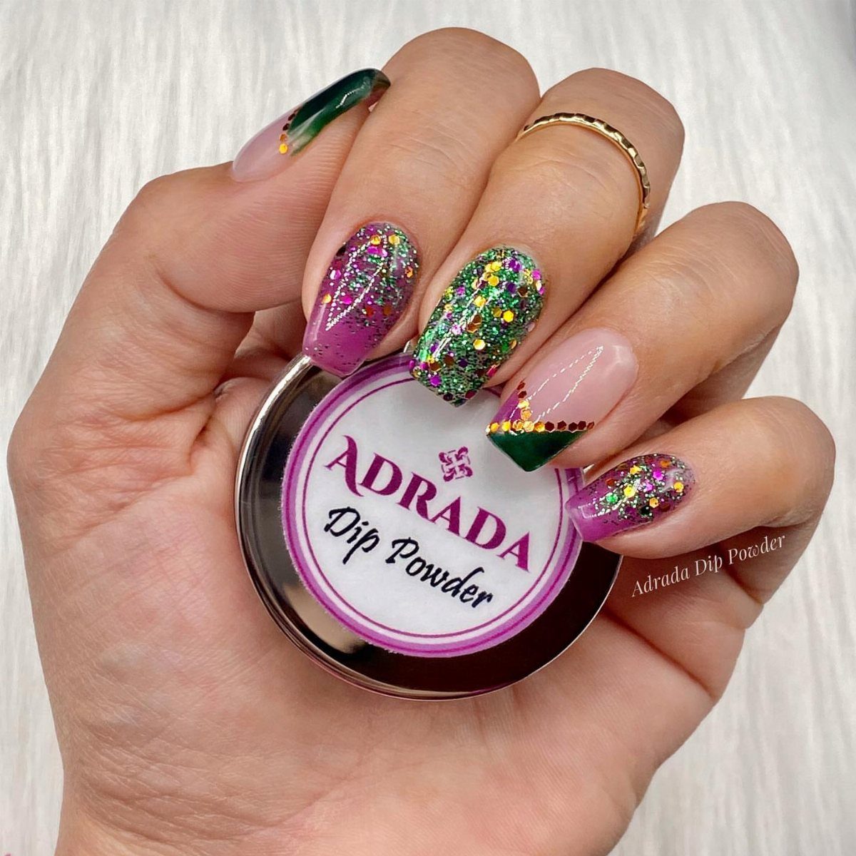 Manicured nails in purple, green, and gold glitter holding a dip powder jar.