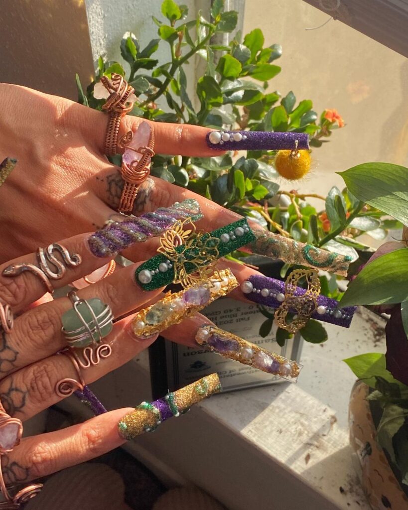 Ornate purple, gold, and green Mardi Gras nail art with pearls and charms.