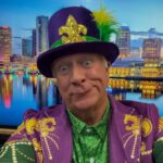 Man in purple and green Mardi Gras costume with a decorated top hat.