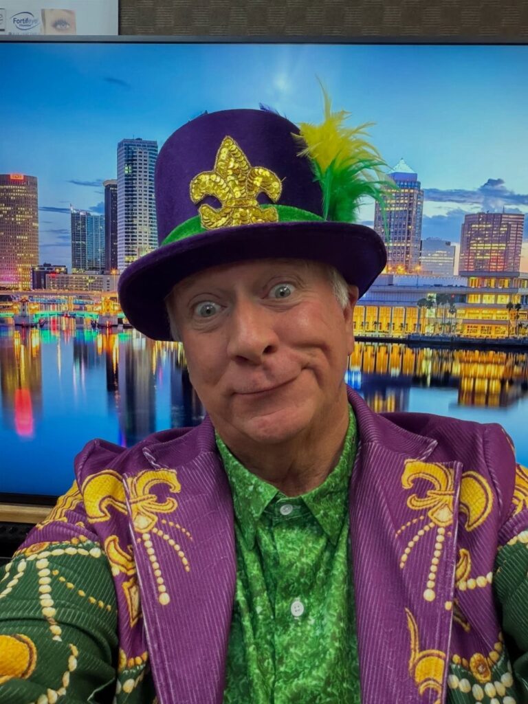 Man in purple and green Mardi Gras costume with a decorated top hat.