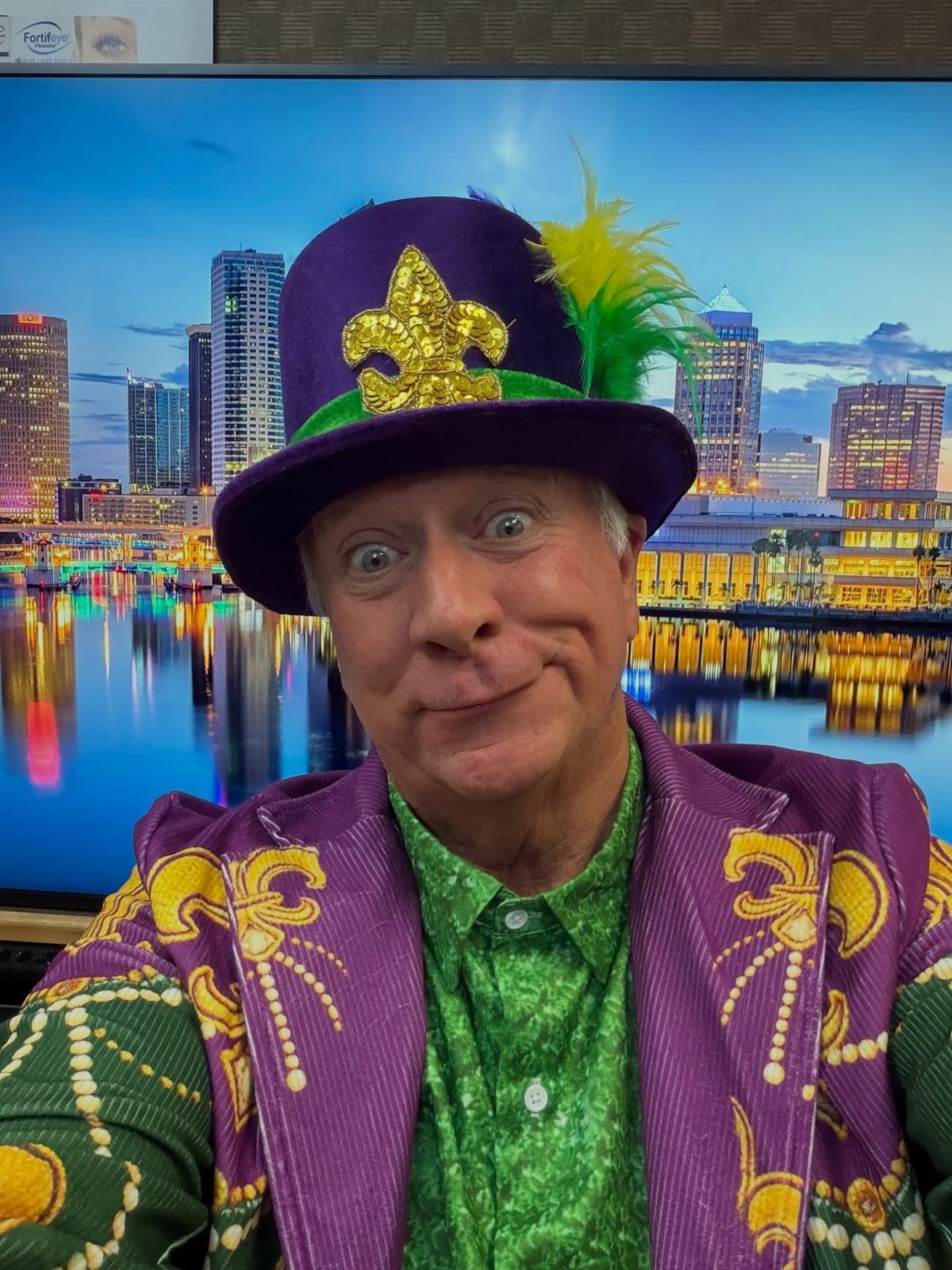 Man in purple and green Mardi Gras costume with a decorated top hat.