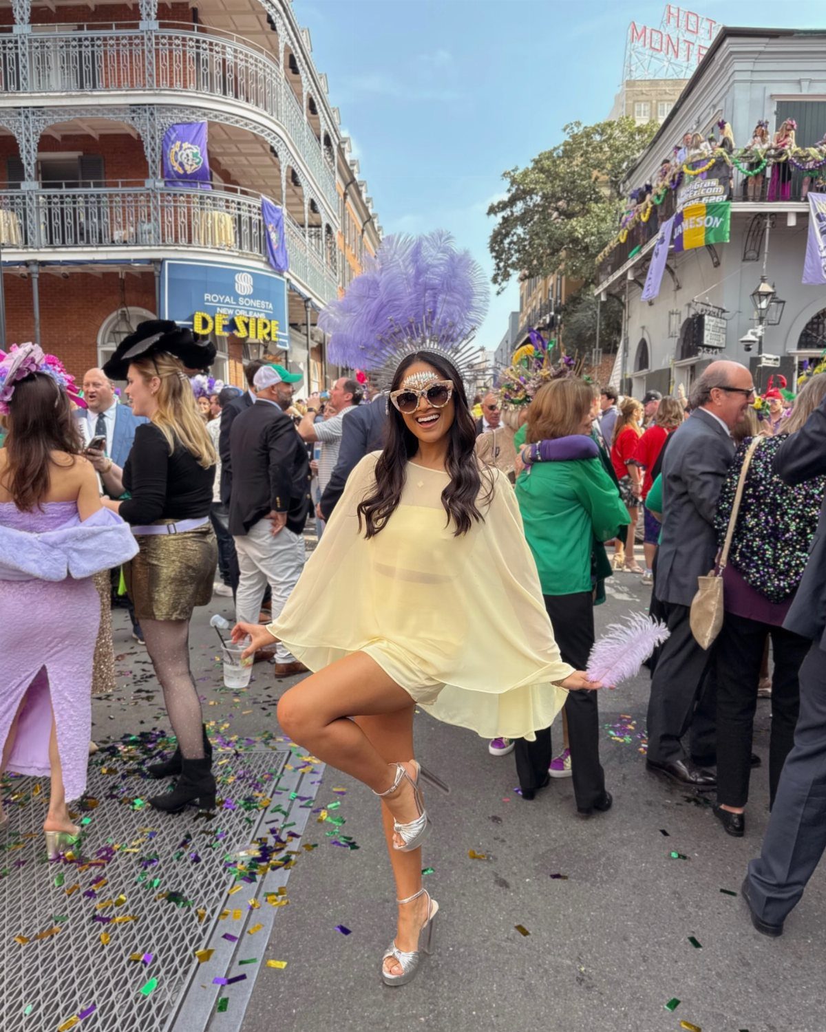 Woman in yellow dress and purple feathered headpiece posing on confetti-covered street