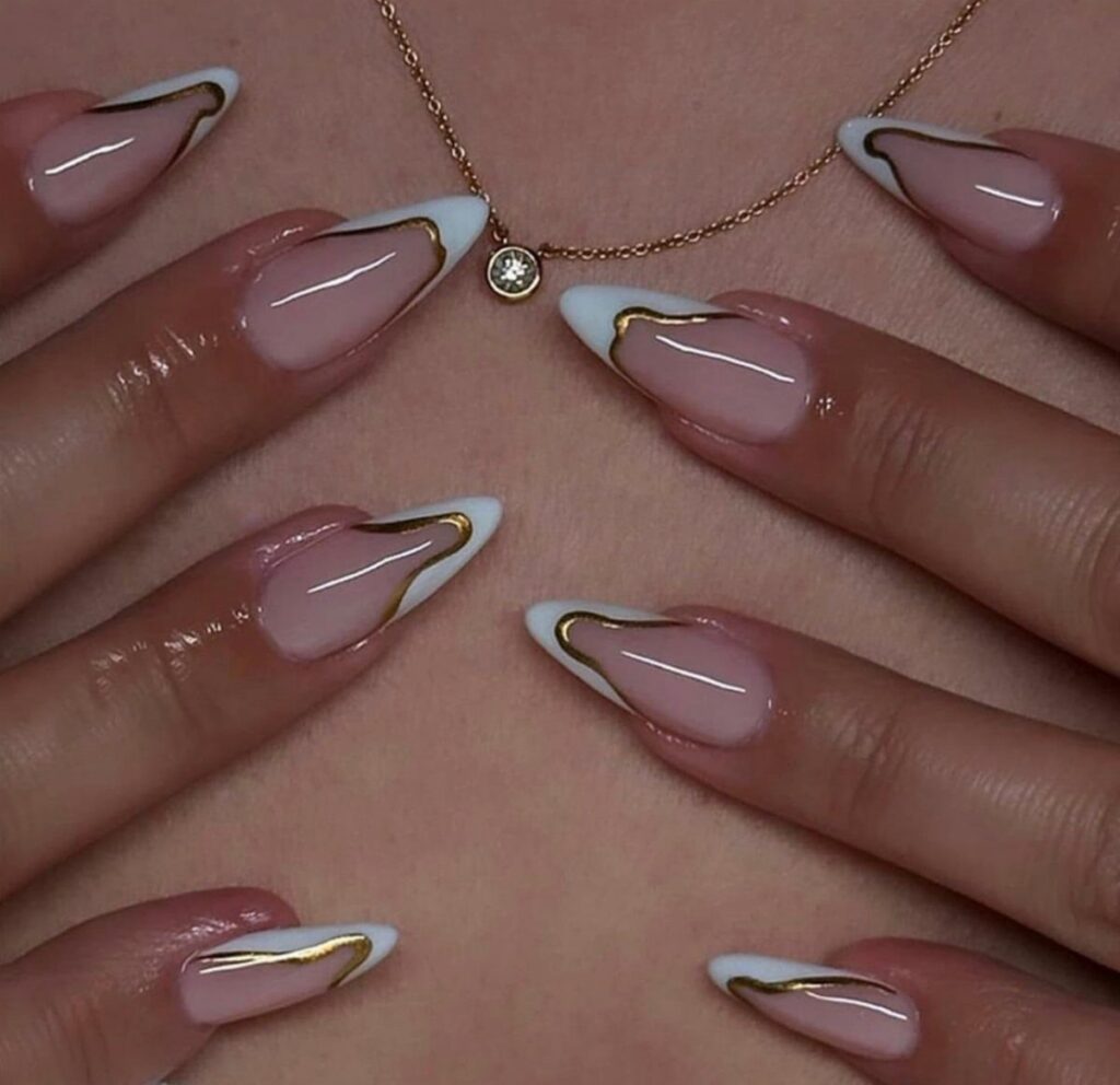 Almond-shaped nails with nude base, white tips, and gold metallic swirl accents.
