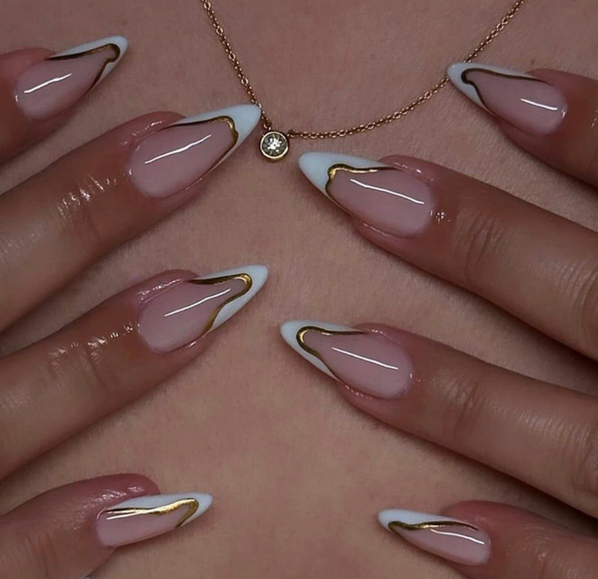 Almond-shaped nails with nude base, white tips, and gold metallic swirl accents.