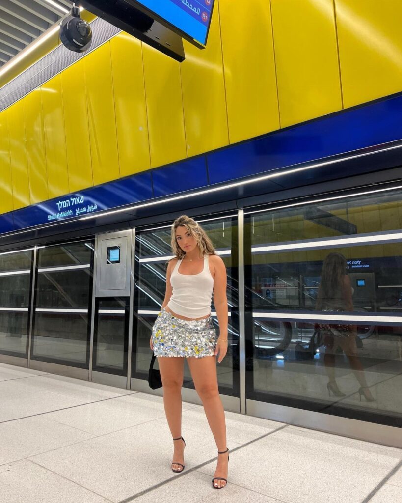 Woman in a silver sequined miniskirt and white tank top at a subway station