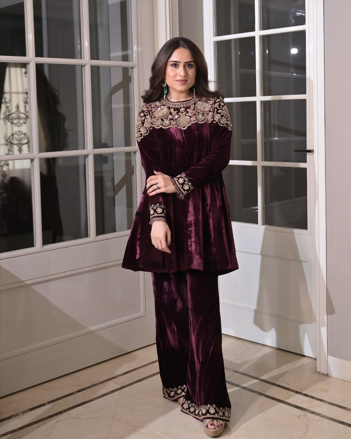 Woman in a purple velvet matching set with gold embroidery standing indoors.