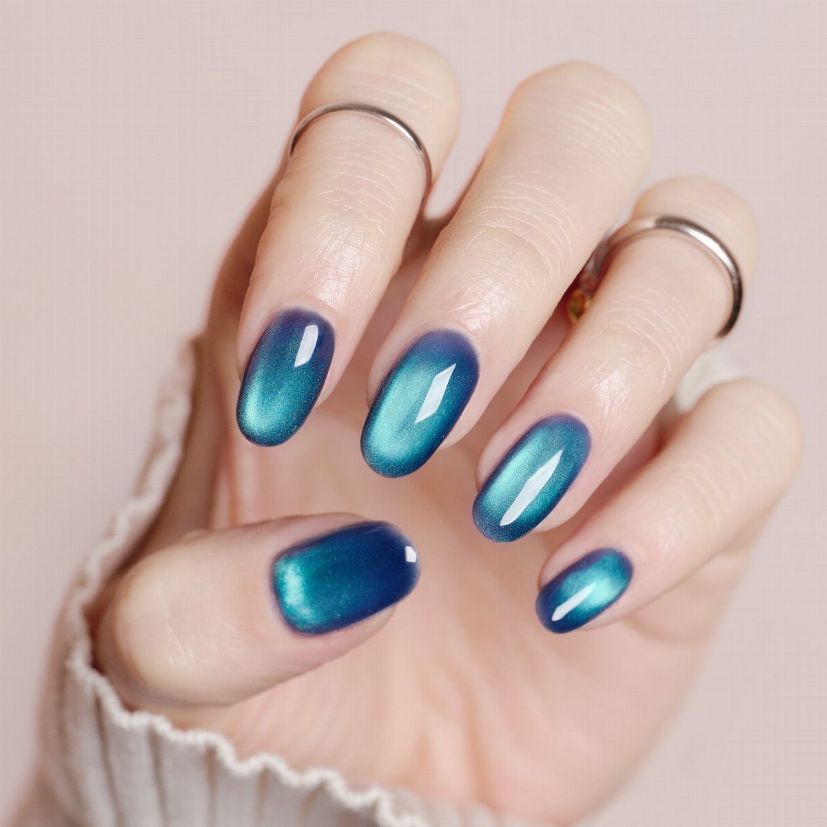 Deep blue and teal shimmering gradient nails on a hand with silver rings.