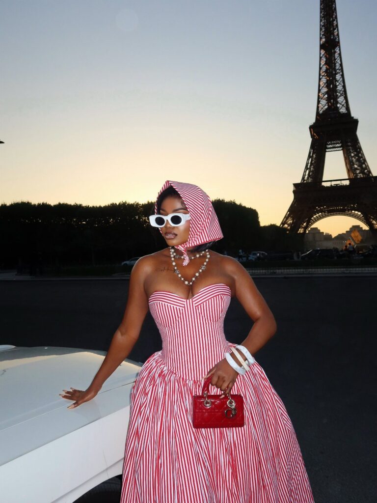 Woman in red and white striped gown and headpiece posing before the Eiffel Tower