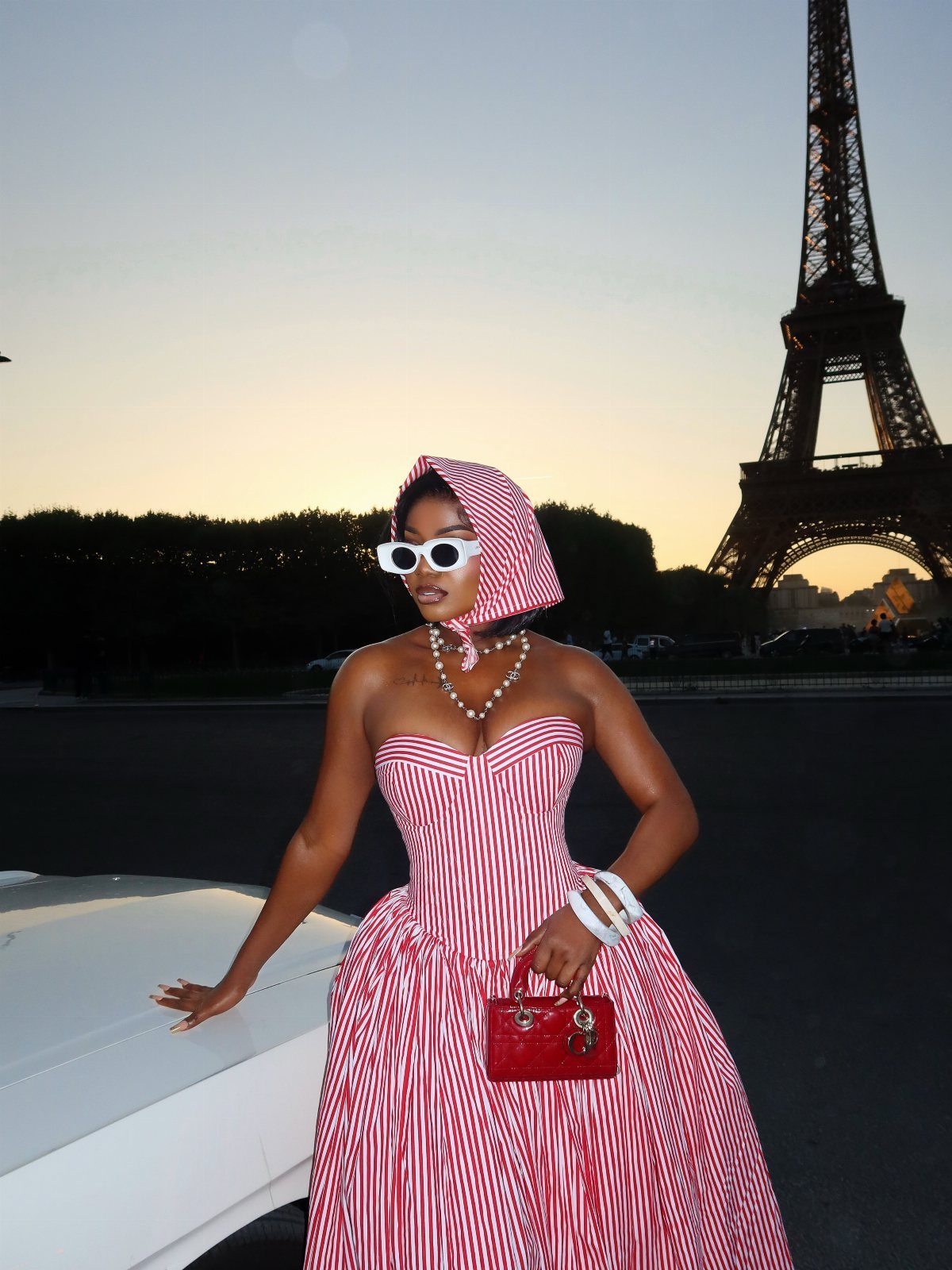 Woman in red and white striped gown and headpiece posing before the Eiffel Tower