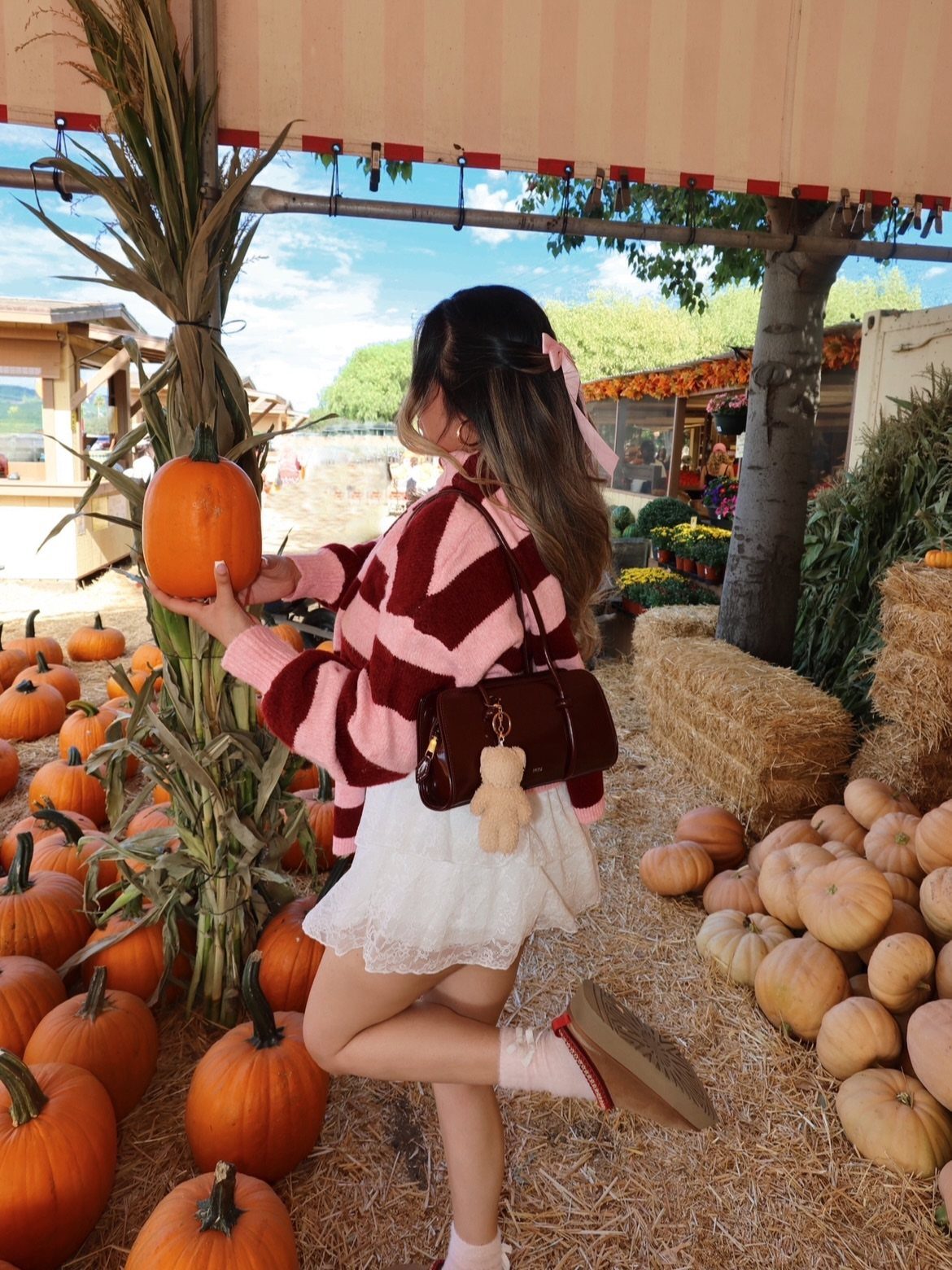 Woman in a red patterned cozy sweater holding a pumpkin in a patch.