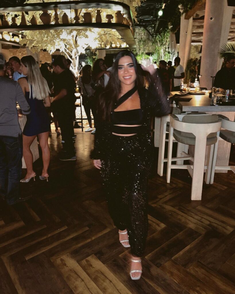 Woman wearing a black sequined crop top and trousers in a lounge setting.
