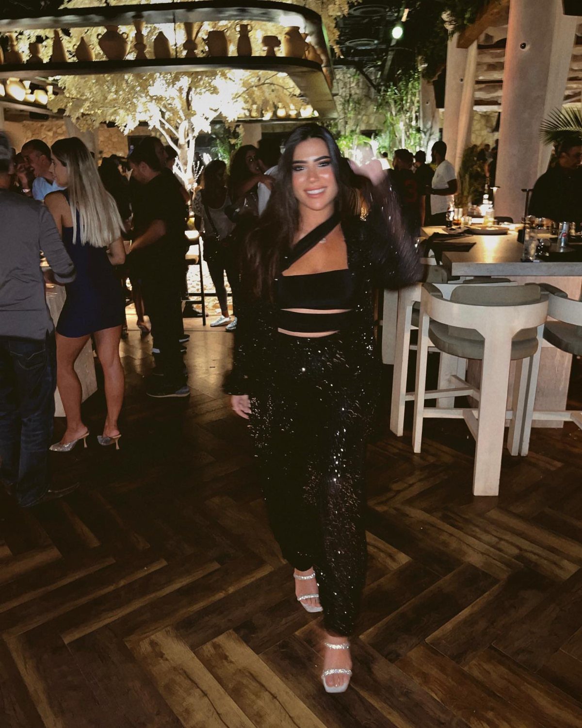 Woman wearing a black sequined crop top and trousers in a lounge setting.
