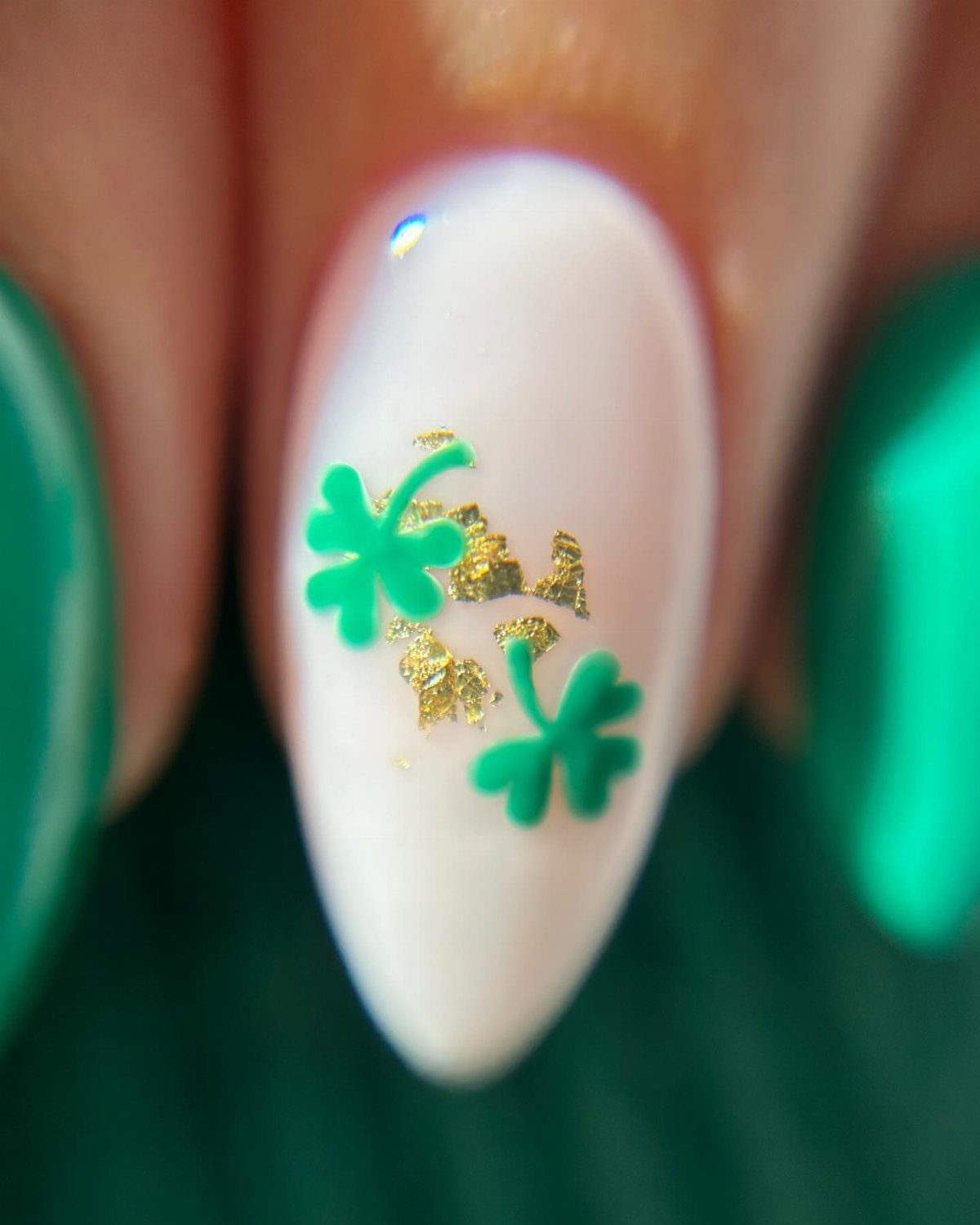 White almond-shaped nail with green shamrocks and gold foil accents and green nails.
