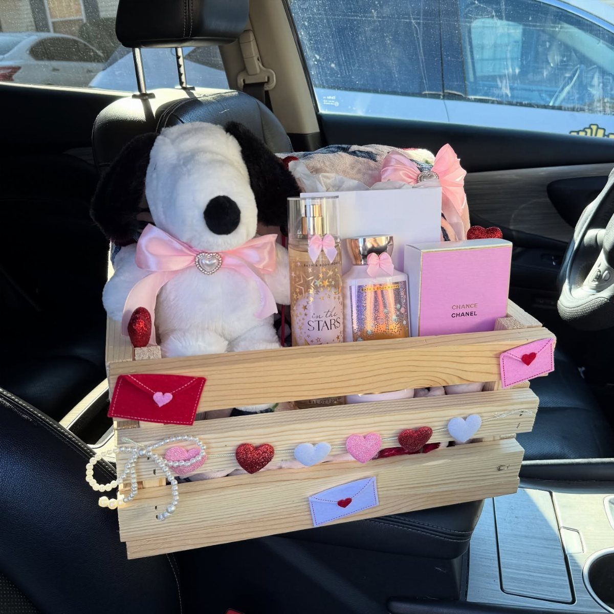 Wooden gift crate with plush dog, perfume, and hearts on a car seat